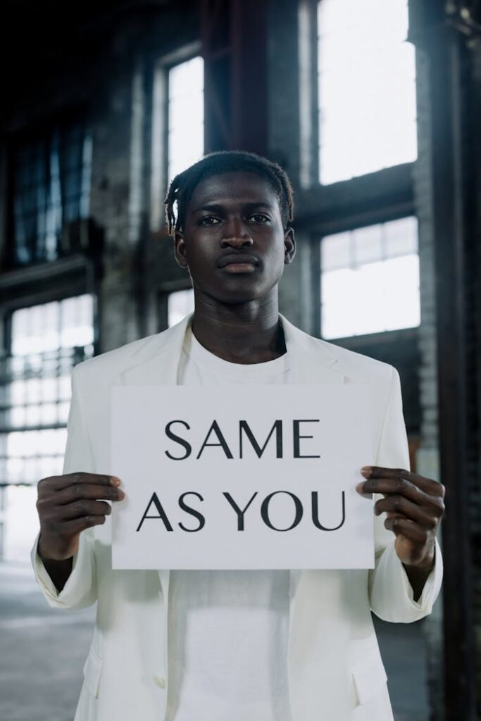 African American man in a white blazer holding an equality sign indoors. Symbolic message conveyed through image.