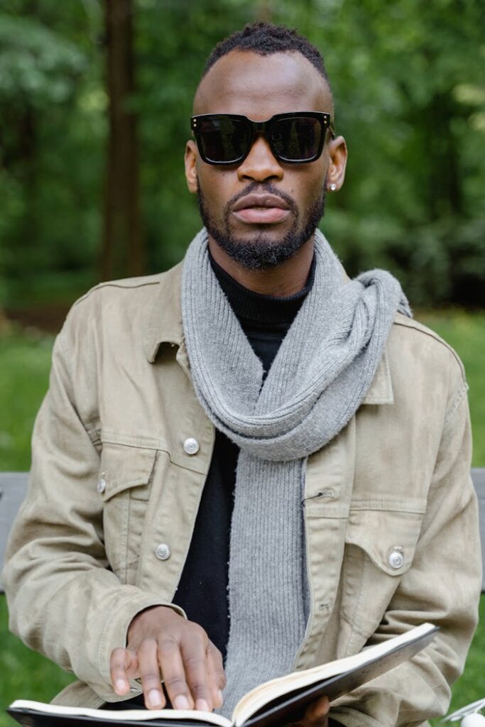 African American man with sunglasses reading a Braille book in a park.